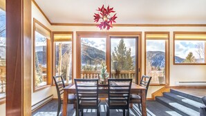 A dining area with a table and chairs, large windows with mountain views, and a red leaf chandelier. - Tennis Townhome #1337 by Summit County Mountain Retreats (Keystone)