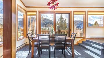 A dining area with a table and chairs, large windows with mountain views, and a red leaf chandelier.