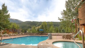 Una piscina con hidromasaje, sillas de descanso y vistas a una cadena montañosa boscosa.