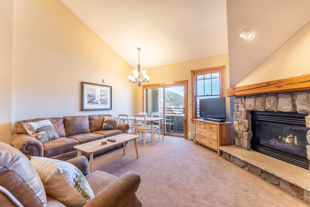 A living room with a stone fireplace, leather sofa, wooden coffee table, and a TV.
