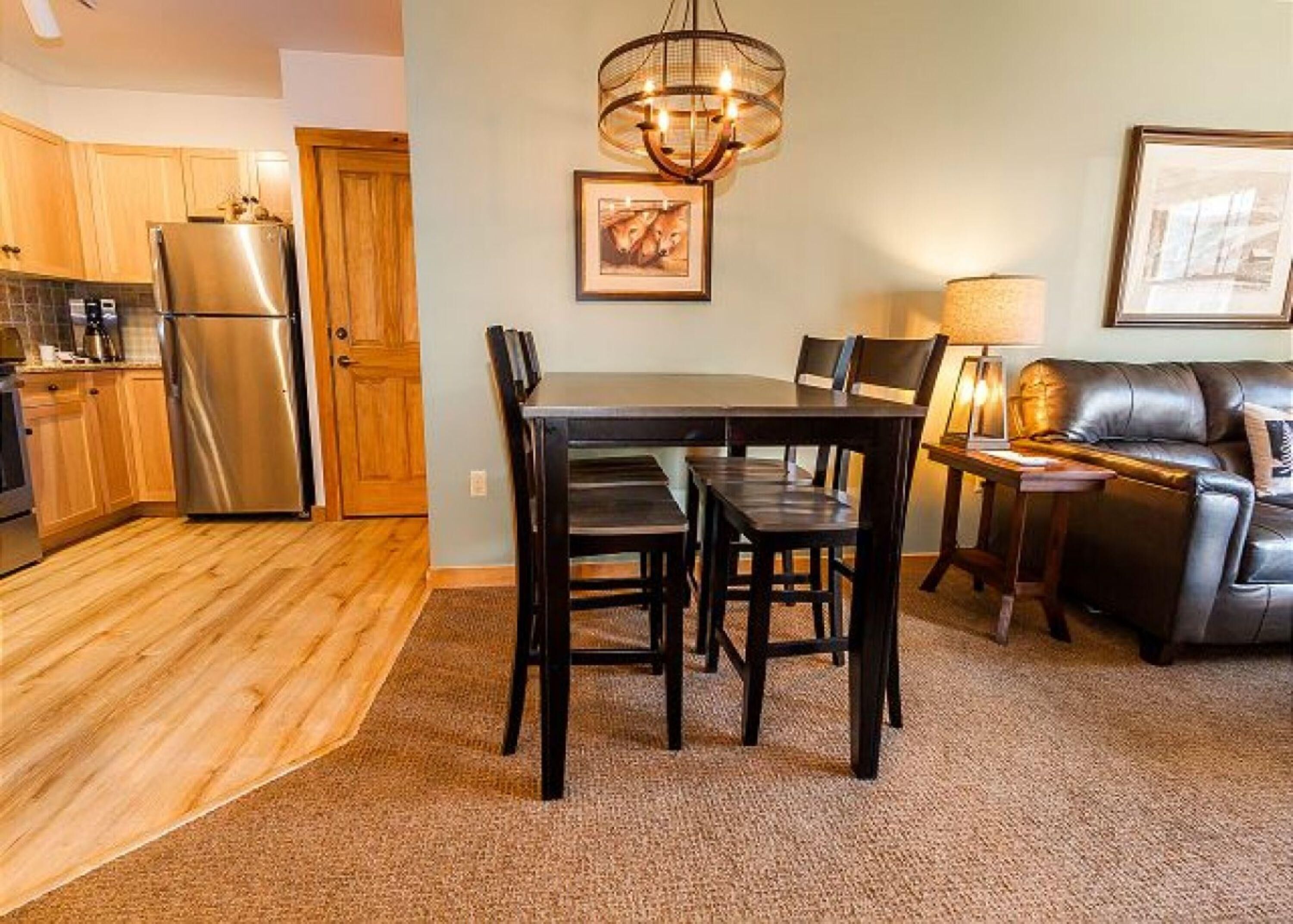 A modern kitchen with wooden cabinets, a stainless steel refrigerator, and a dining area with a dark wooden table and chairs.