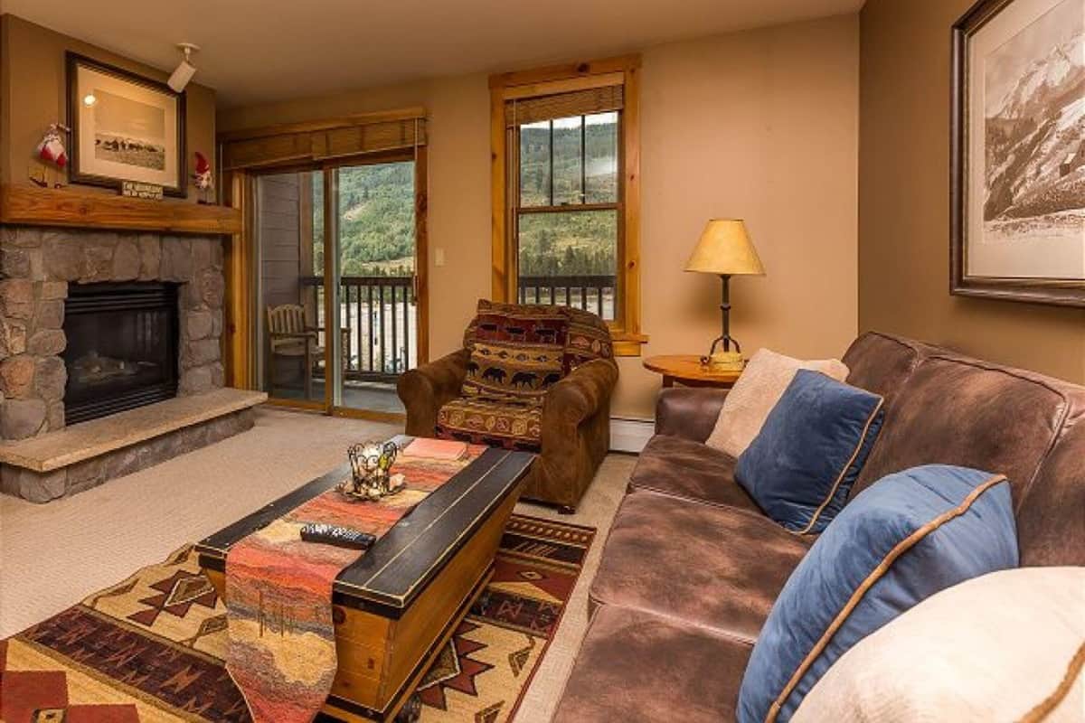 A cozy living room with a stone fireplace, a leather couch, and a patterned rug.