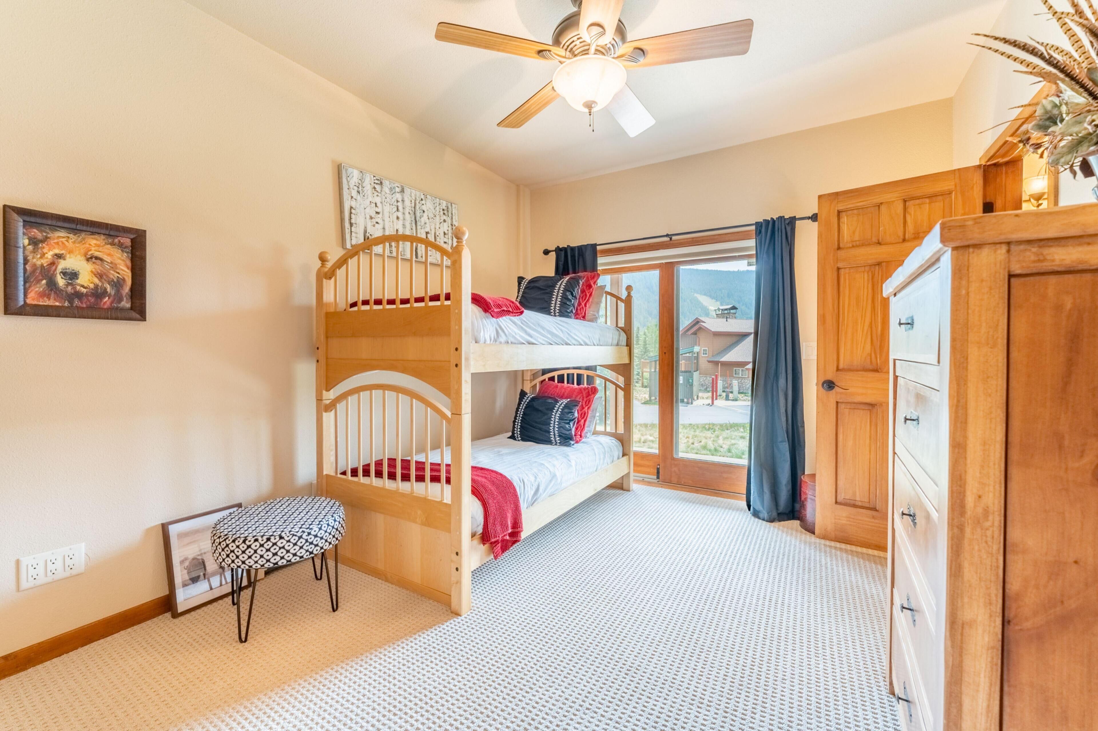 A bedroom with a bunk bed, a wooden dresser, a ceiling fan, and a view through a glass door.