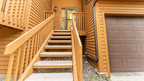 Un escalier en bois mène à une porte d’entrée, avec une porte de garage située sur le côté droit.