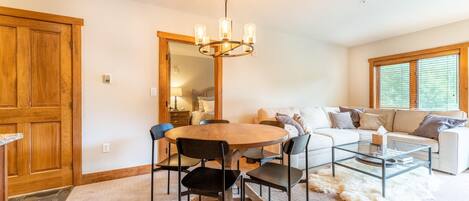 A dining area with a round table, chairs, a chandelier, and a sofa in the background.