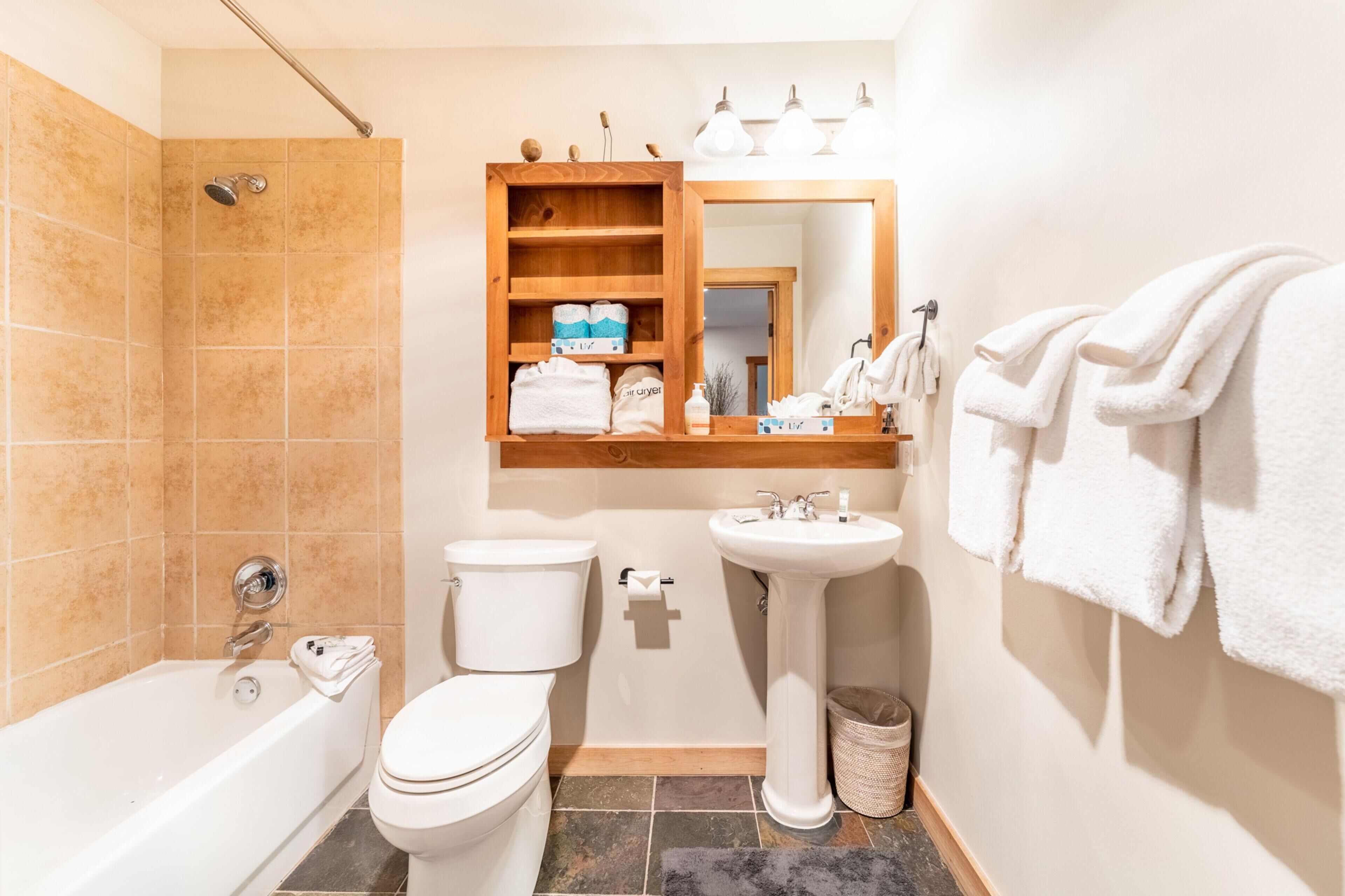 Une salle de bain avec une baignoire, des toilettes, un lavabo et une étagère en bois où sont posées des serviettes.