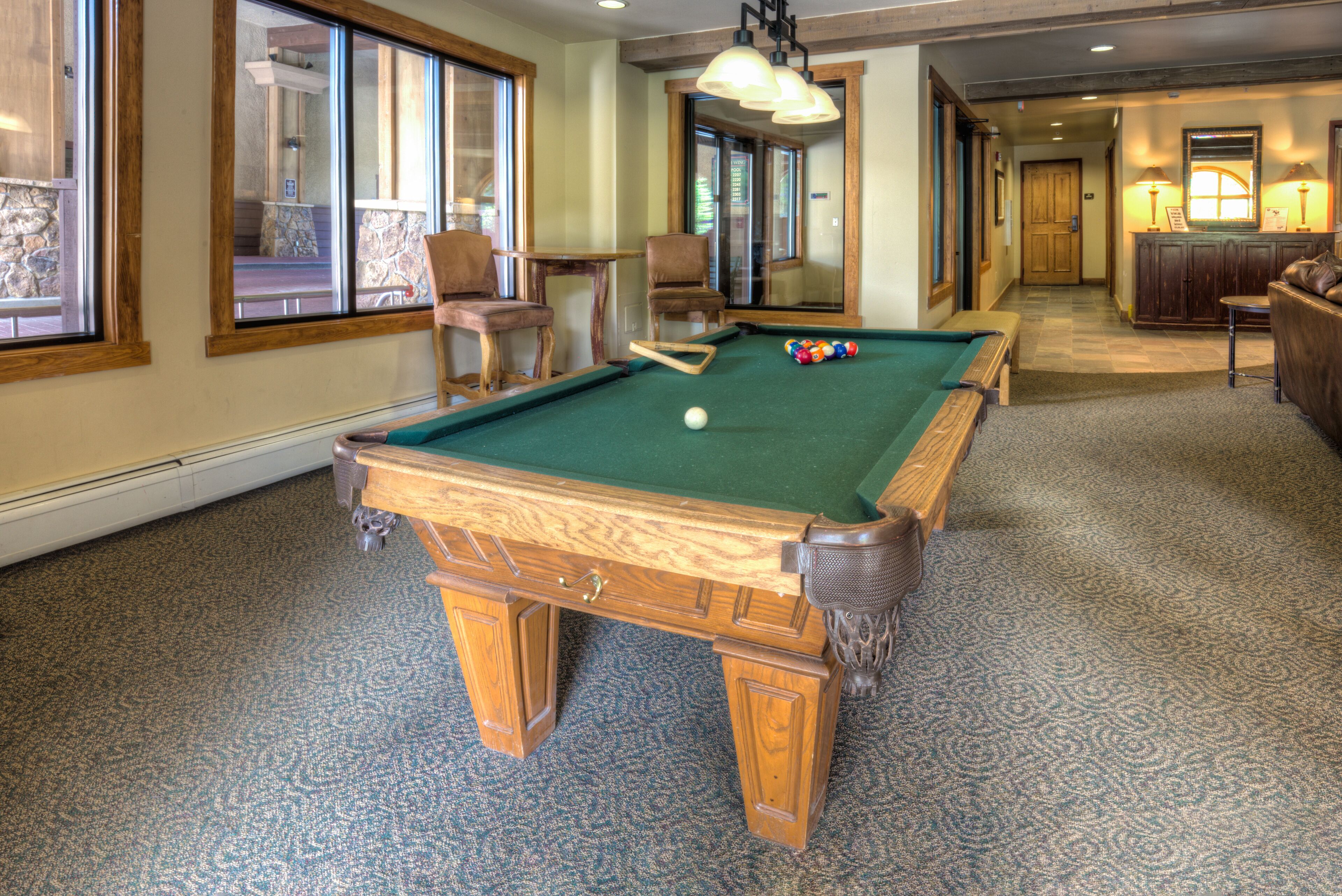 A pool table in a room with large windows, a chair, and a lamp.