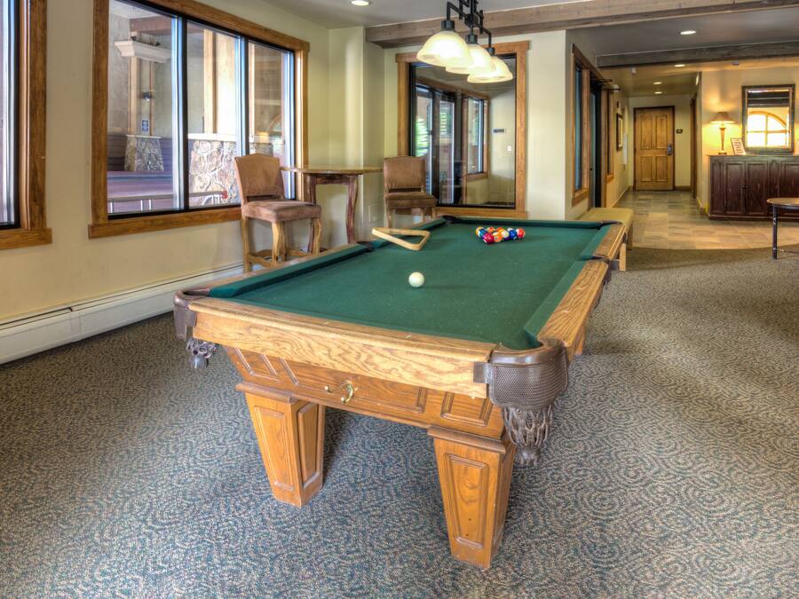 A pool table in a room with large windows, a chair, and a lamp.