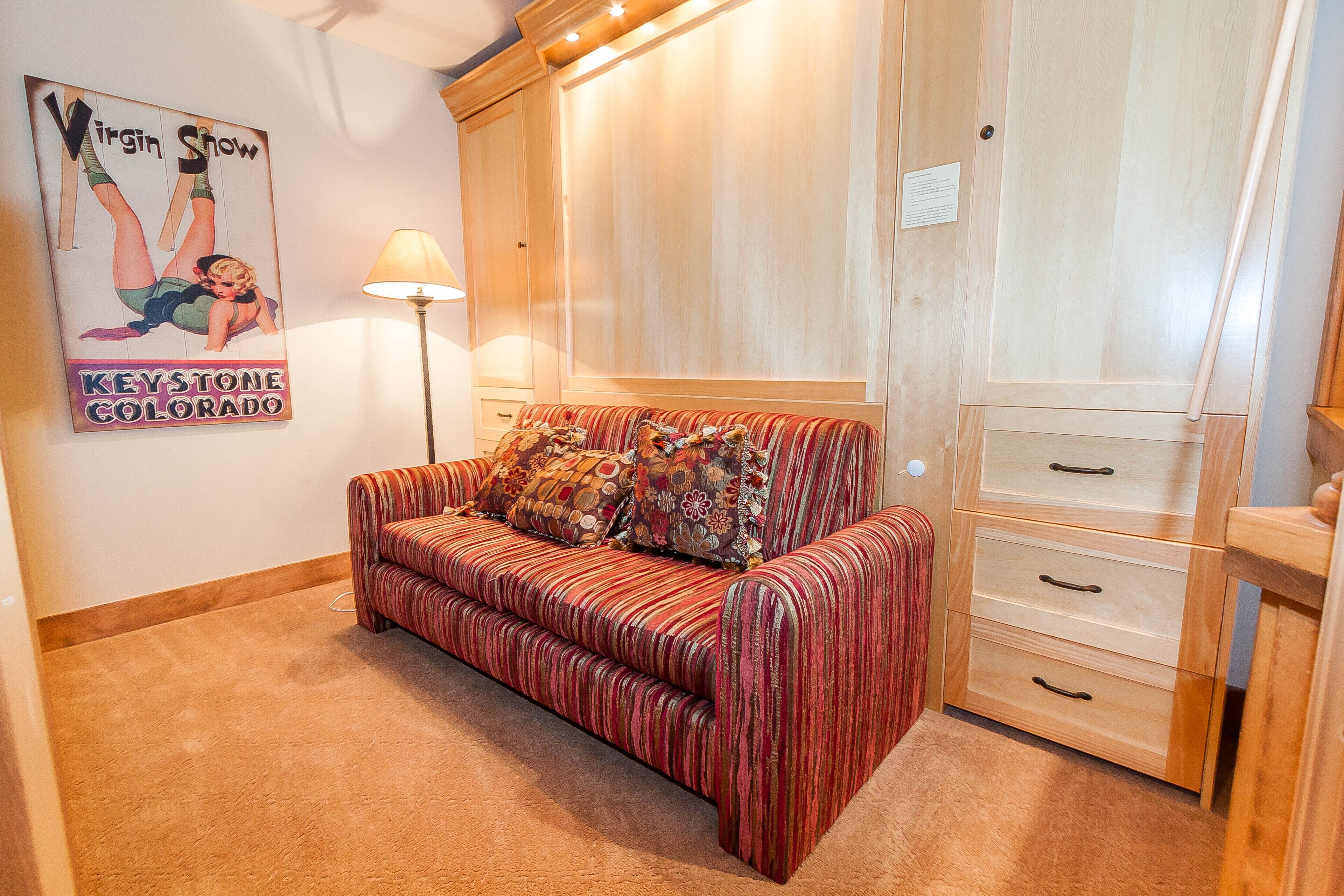 A room with a striped sofa, a lamp, a wardrobe, and a poster on the wall.