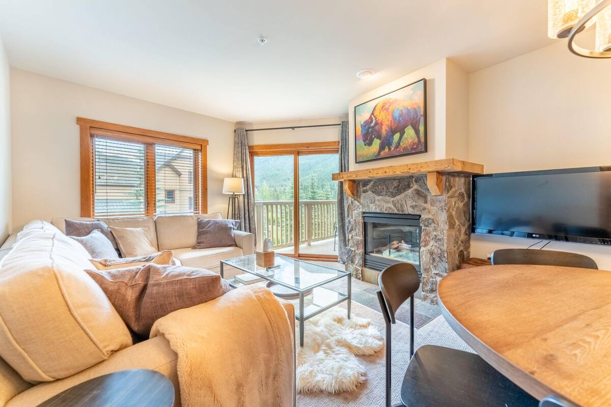 A cozy living room with a stone fireplace, a flat-screen TV, and a comfortable seating area with a sofa and chairs.