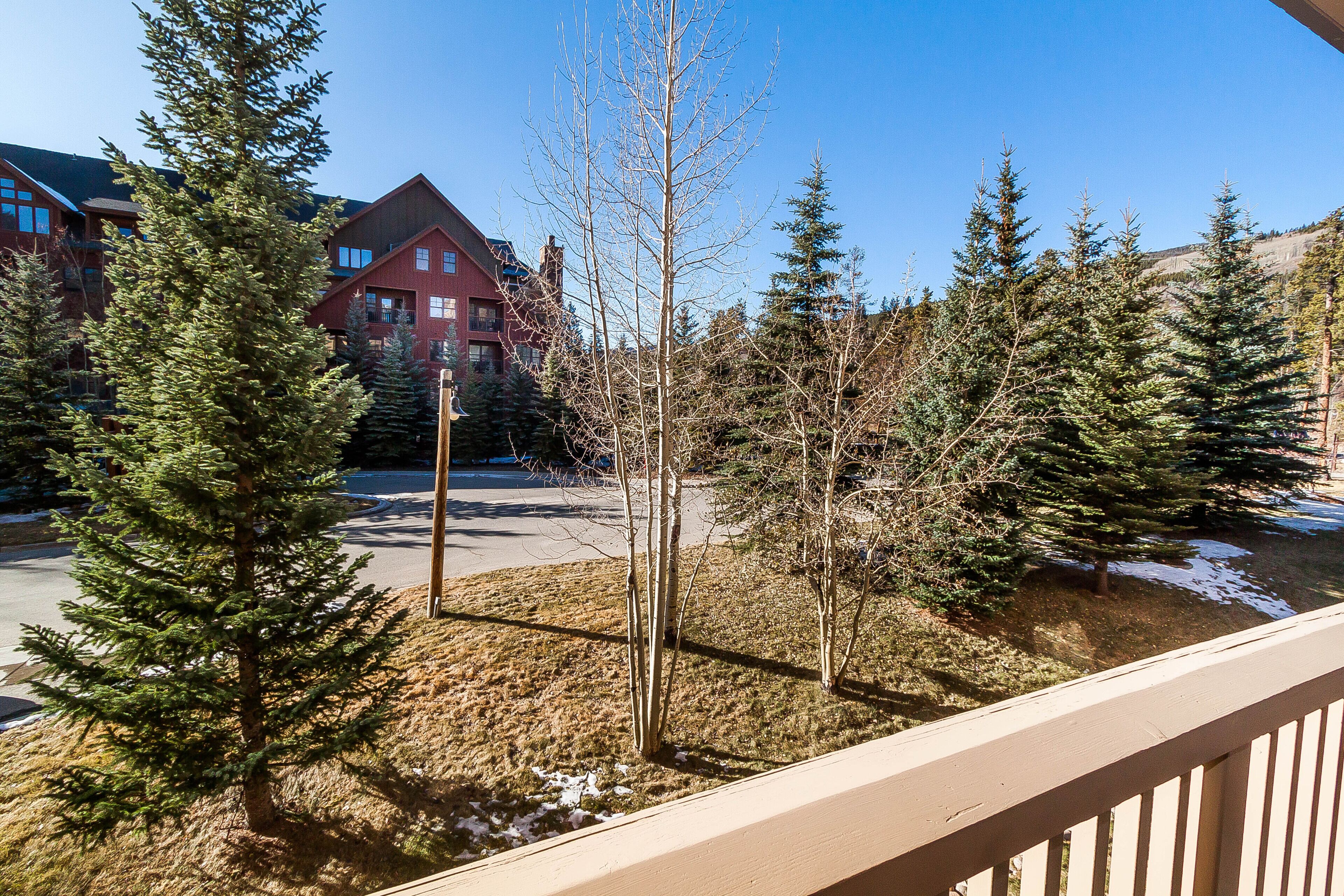 A view of a building with multiple windows and a red roof, surrounded by evergreen trees and a clear blue sky.