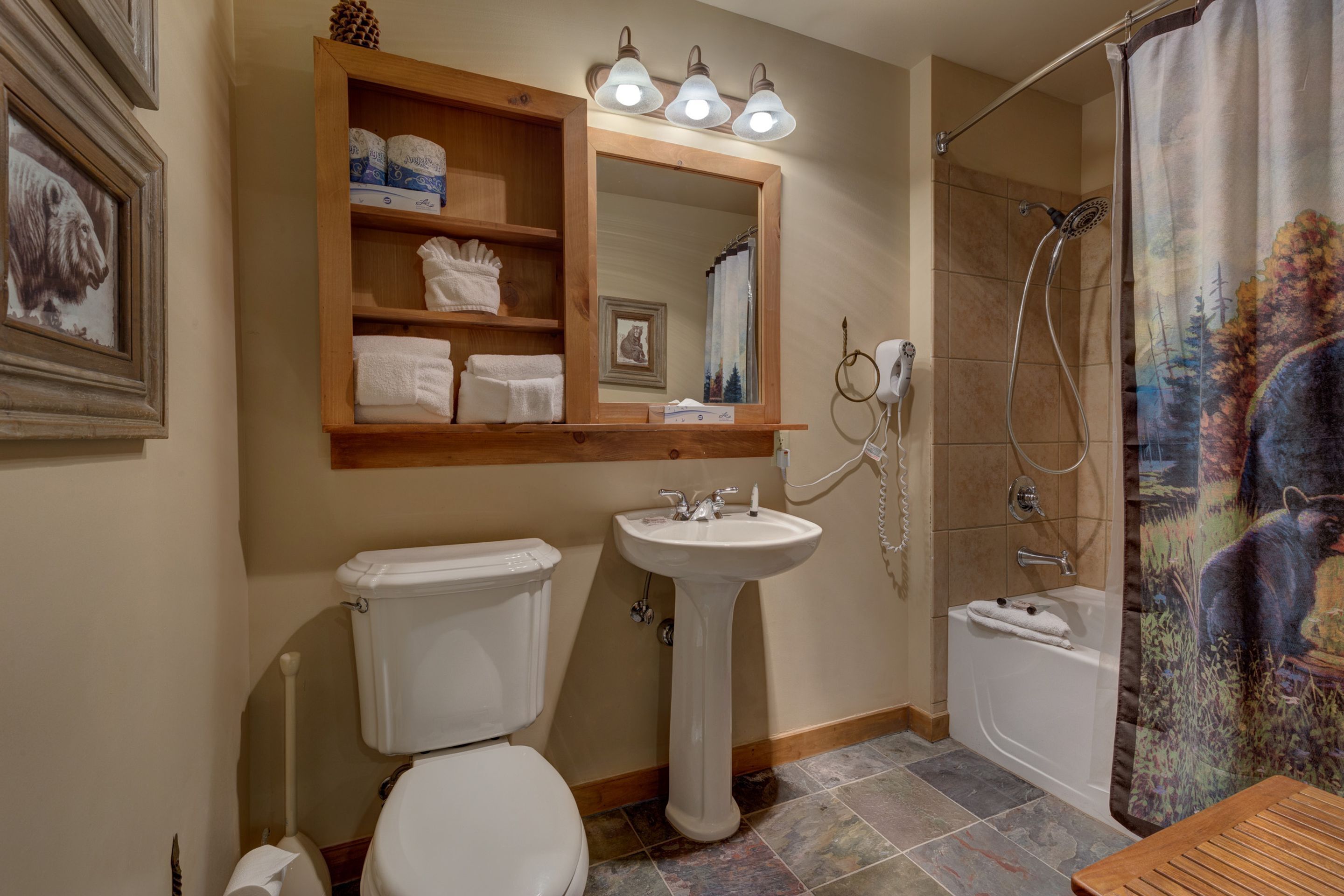 A bathroom with a toilet, sink, and shower. There is a mirror above the sink with shelves holding towels and toiletries.