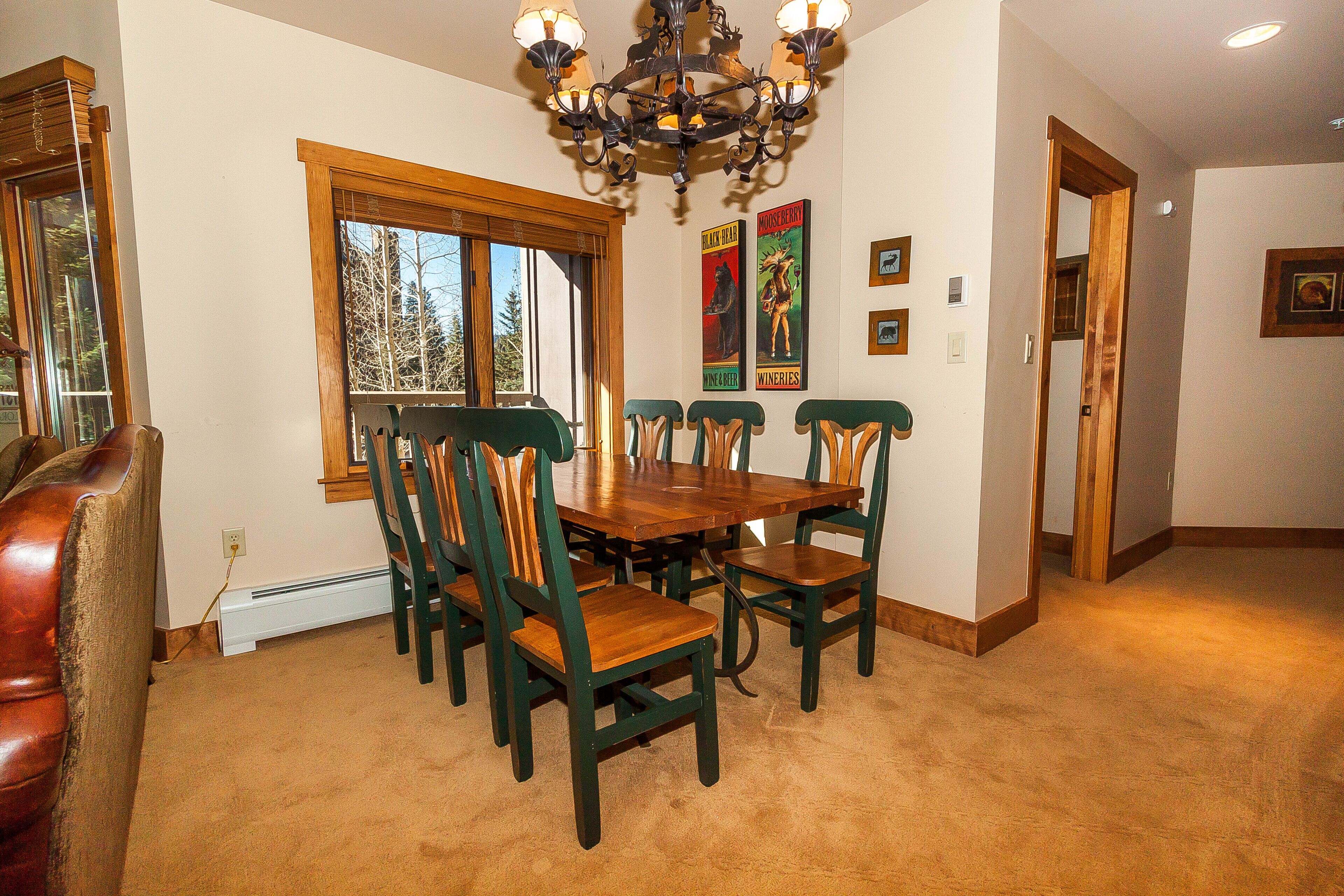 A dining area with a wooden table and chairs, a chandelier, and a window with blinds.