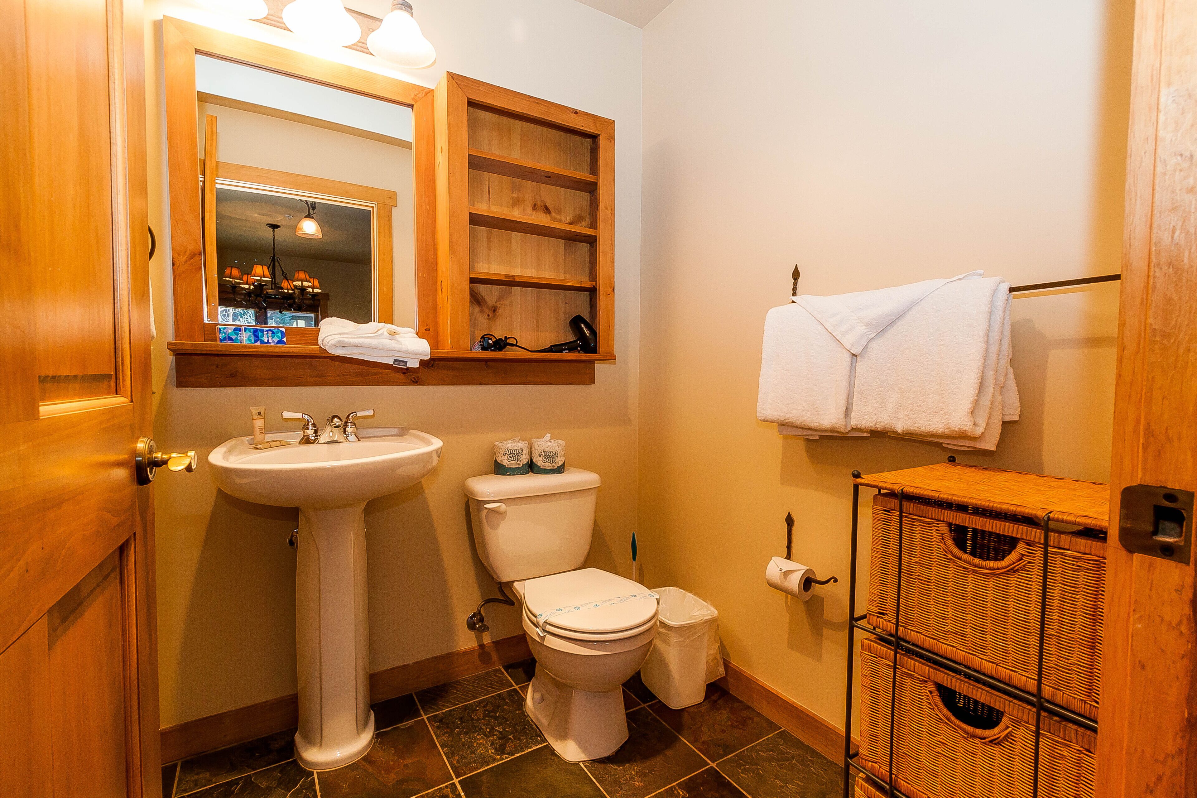 A bathroom with a wooden vanity, a sink, a toilet, and a wicker storage unit.