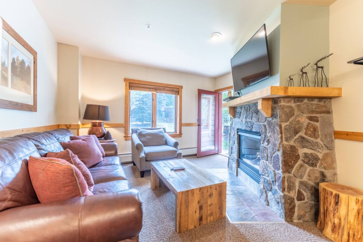 A cozy living room with a stone fireplace, leather sofa, and a flat-screen TV mounted above it.
