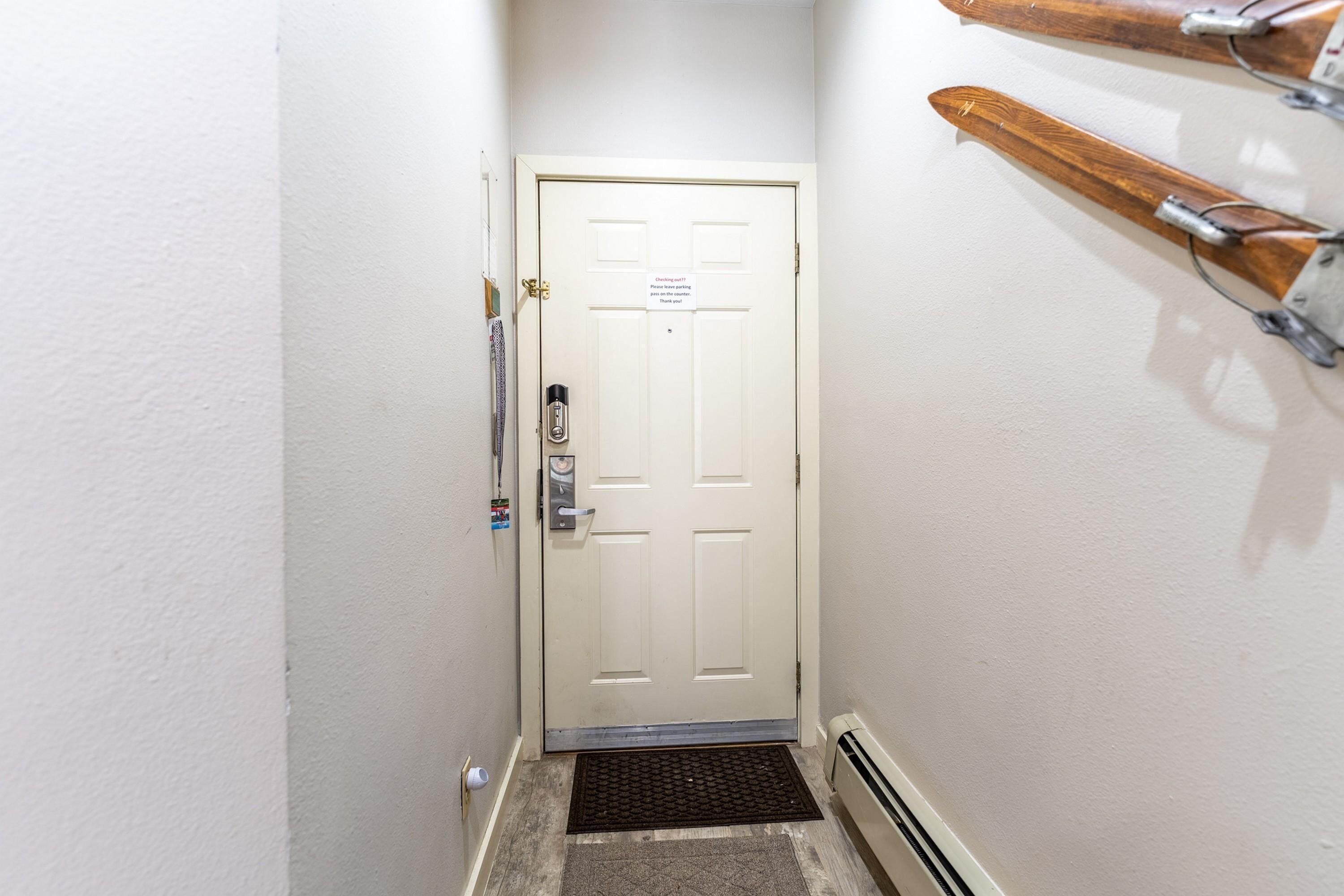 A narrow hallway with a white door, a doormat, and a wall-mounted coat rack.