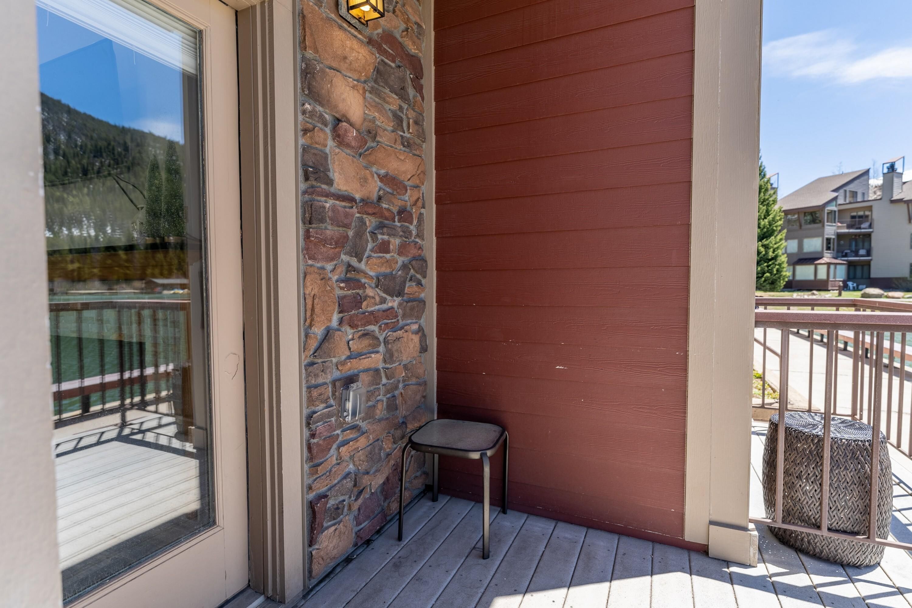 A balcony with a stone wall, a small stool, and a view of a lake and buildings.