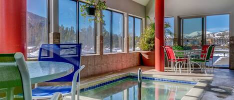 An indoor pool area with a view of mountains, a table with chairs, and a hanging plant.