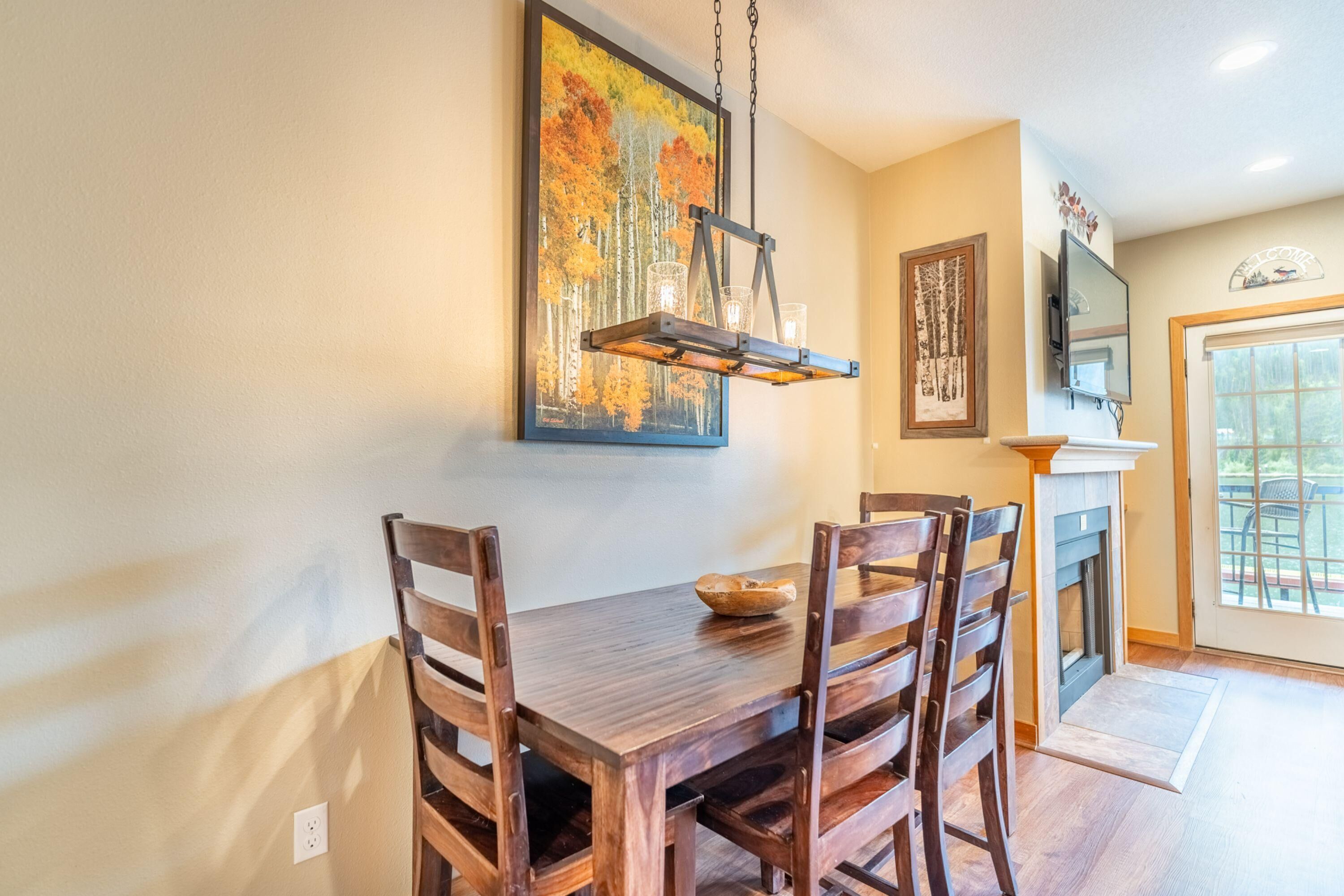 A dining area with a wooden table and chairs, a painting above the table, a fireplace, and a television mounted on the wall.
