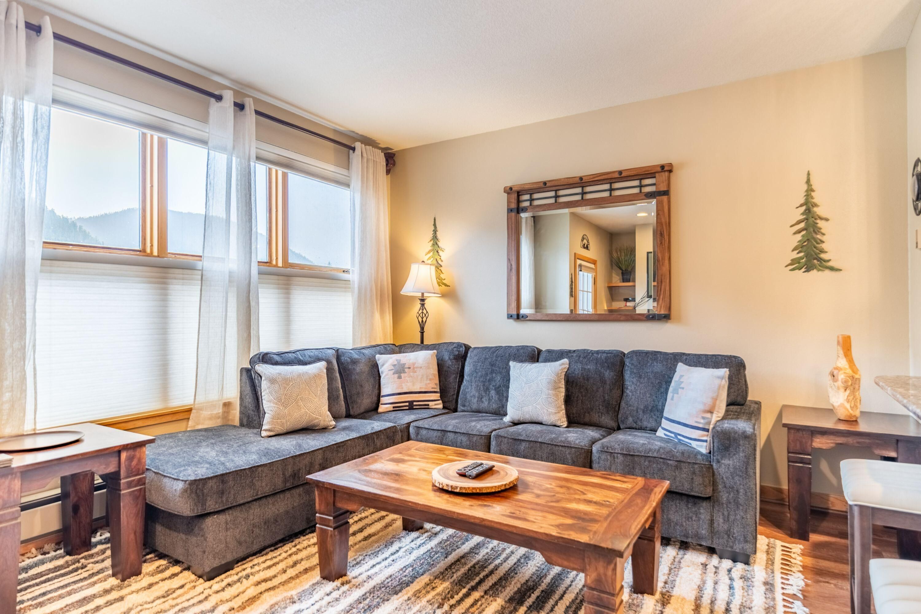 A modern living room with a sectional sofa, a wooden coffee table, and a large mirror on the wall.
