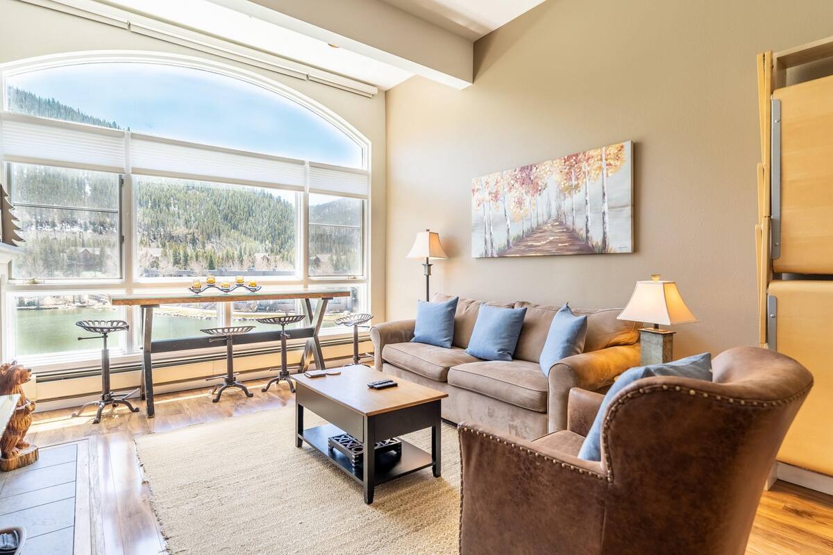 A living room with a large window, a sofa, a coffee table, and a painting on the wall.