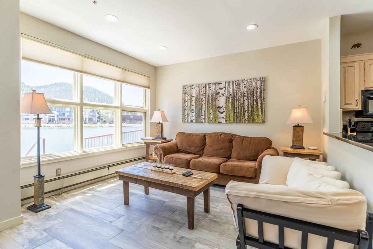 A living room with a brown sofa, a coffee table, and a view of a lake.