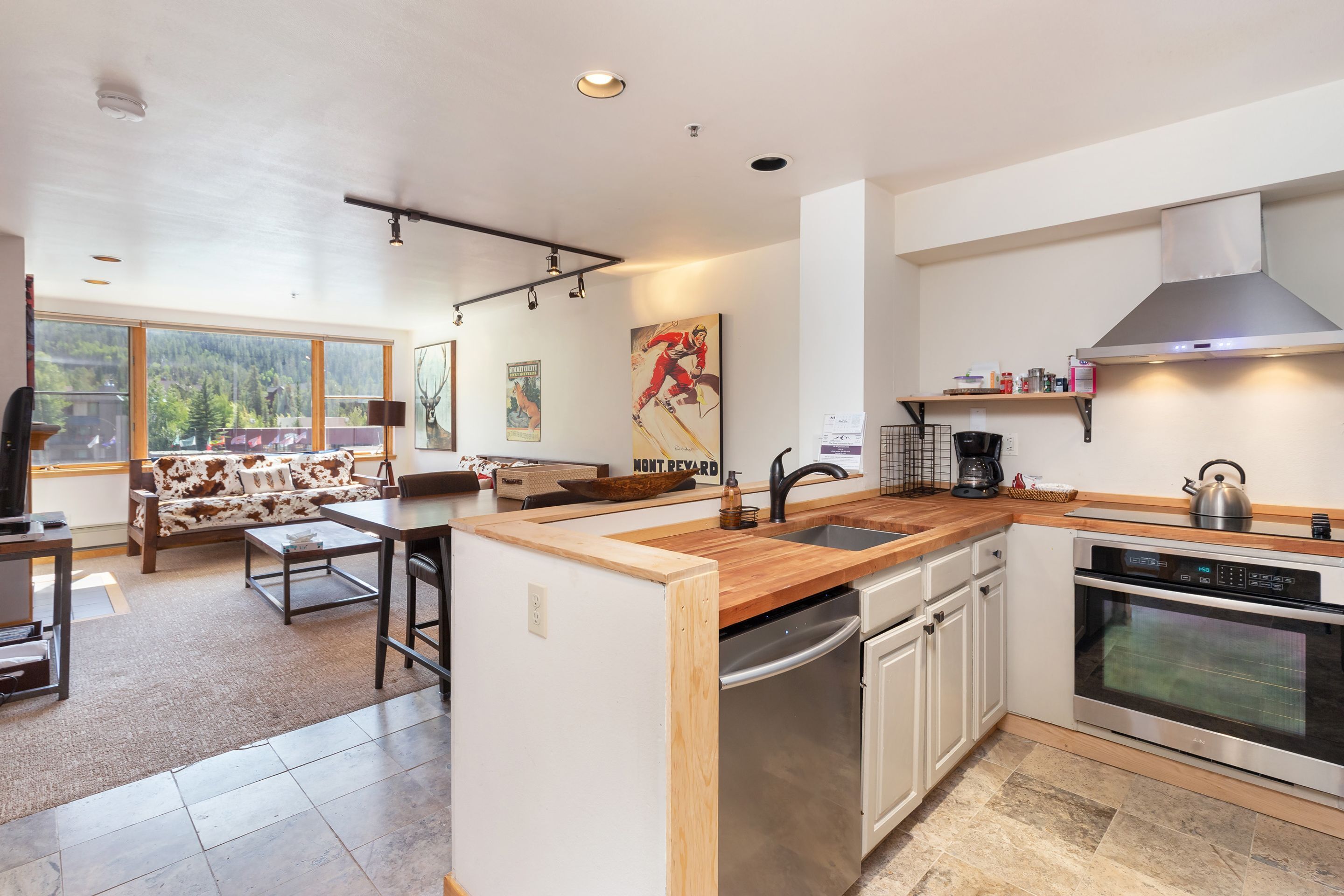 A modern kitchen with a wooden countertop, stainless steel appliances, and a large window offering a view of the outdoors.