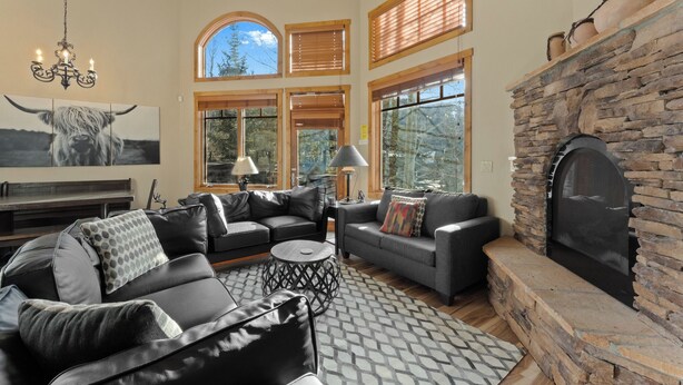 A spacious living room with leather sofas, a stone fireplace, and large windows. - Rasor Court #20 by Summit County Mountain Retreats (Keystone)