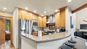 A modern kitchen with granite countertops, stainless steel appliances, wooden cabinets, and a bar area with stools. - Rasor Court #20 by Summit County Mountain Retreats (Keystone)