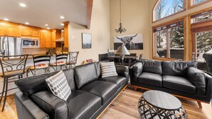 A spacious living area with a black leather sofa, a dining table with chairs, and a chandelier. - Rasor Court #20 by Summit County Mountain Retreats (Keystone)