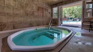 Ett spaområde med ett bubbelbad, stenmurar och utsikt över en pool och träd utanför.
