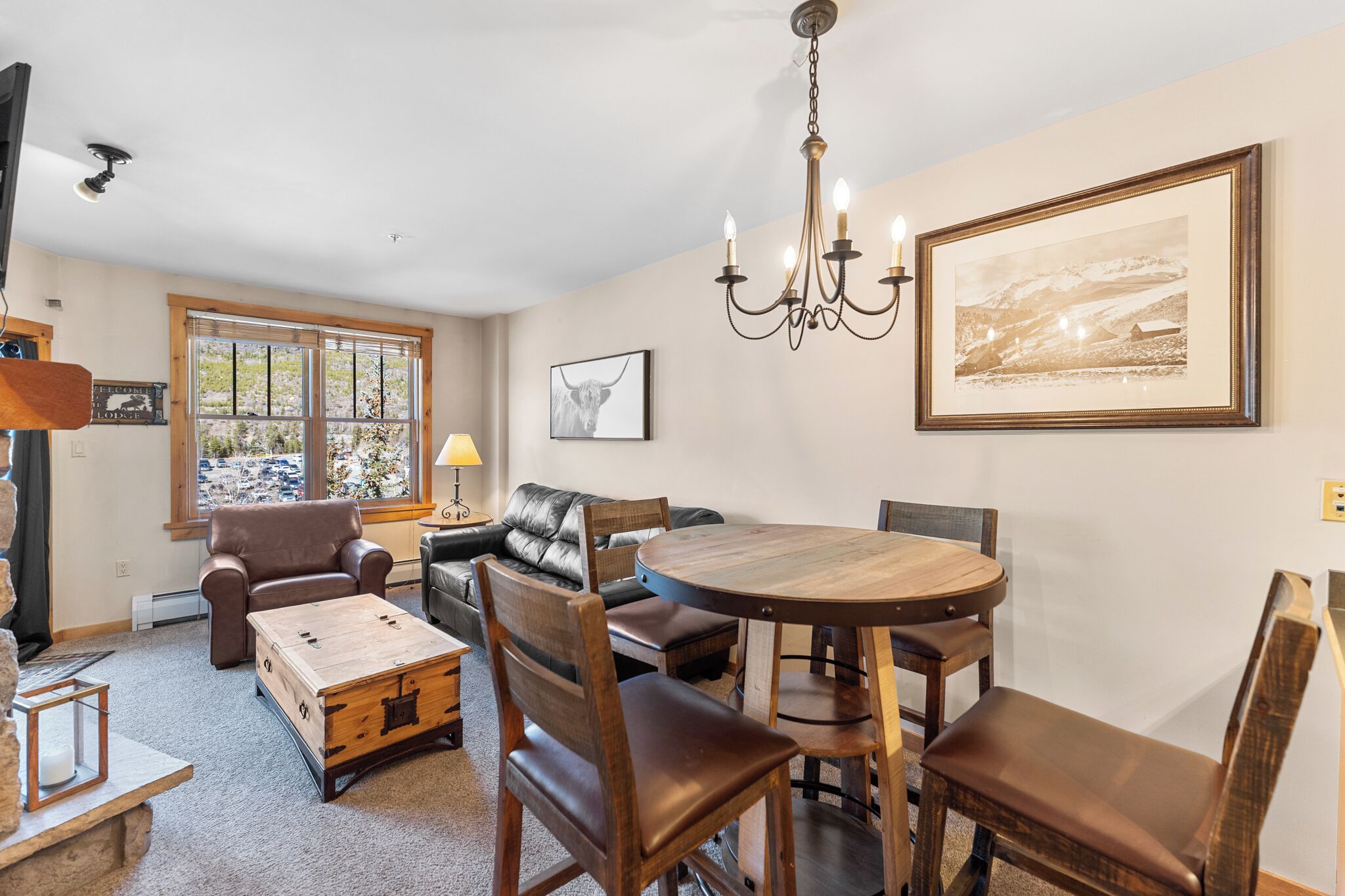 A cozy living room with a wooden coffee table, leather sofas, a round dining table, and a chandelier.