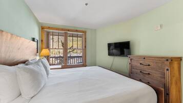 Un dormitorio con cama, cómoda de madera, televisor y ventana con persianas.