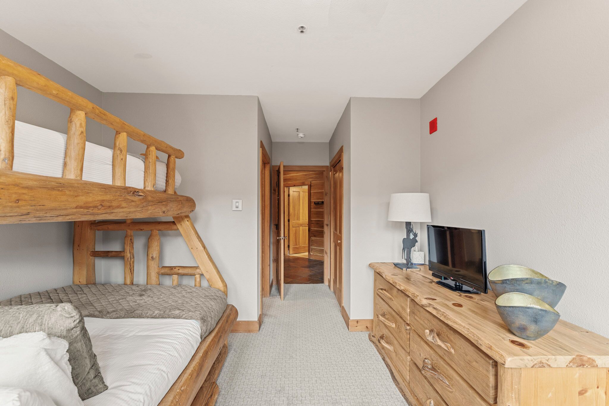 A room with a bunk bed, a wooden dresser, a television, and a hallway leading to a wooden door.