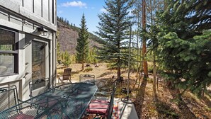 En uteplats med ett metallbord och stolar, omgiven av ett skogsområde och med ett berg i bakgrunden.