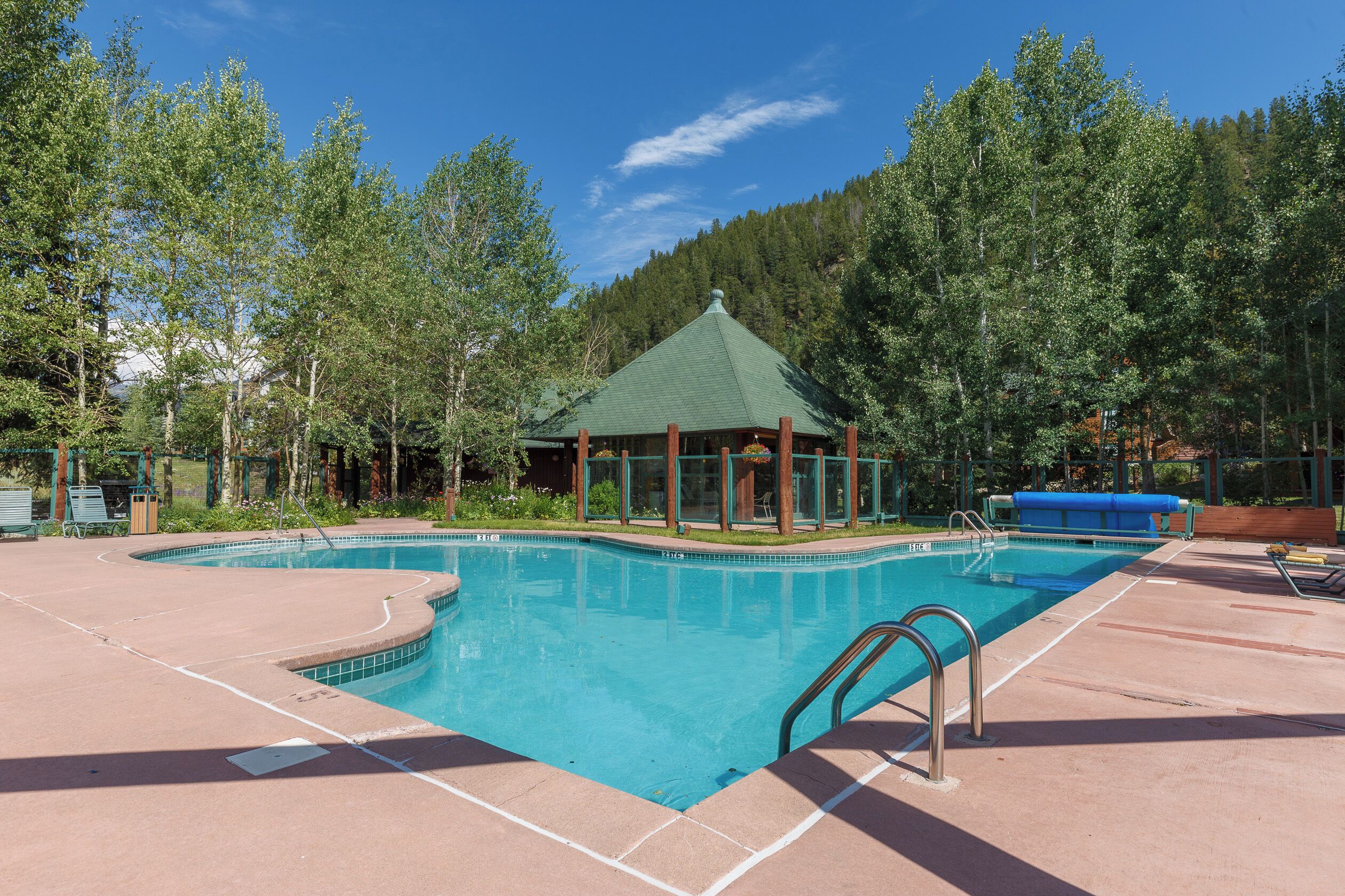 A swimming pool with a gazebo, surrounded by trees and a clear sky.