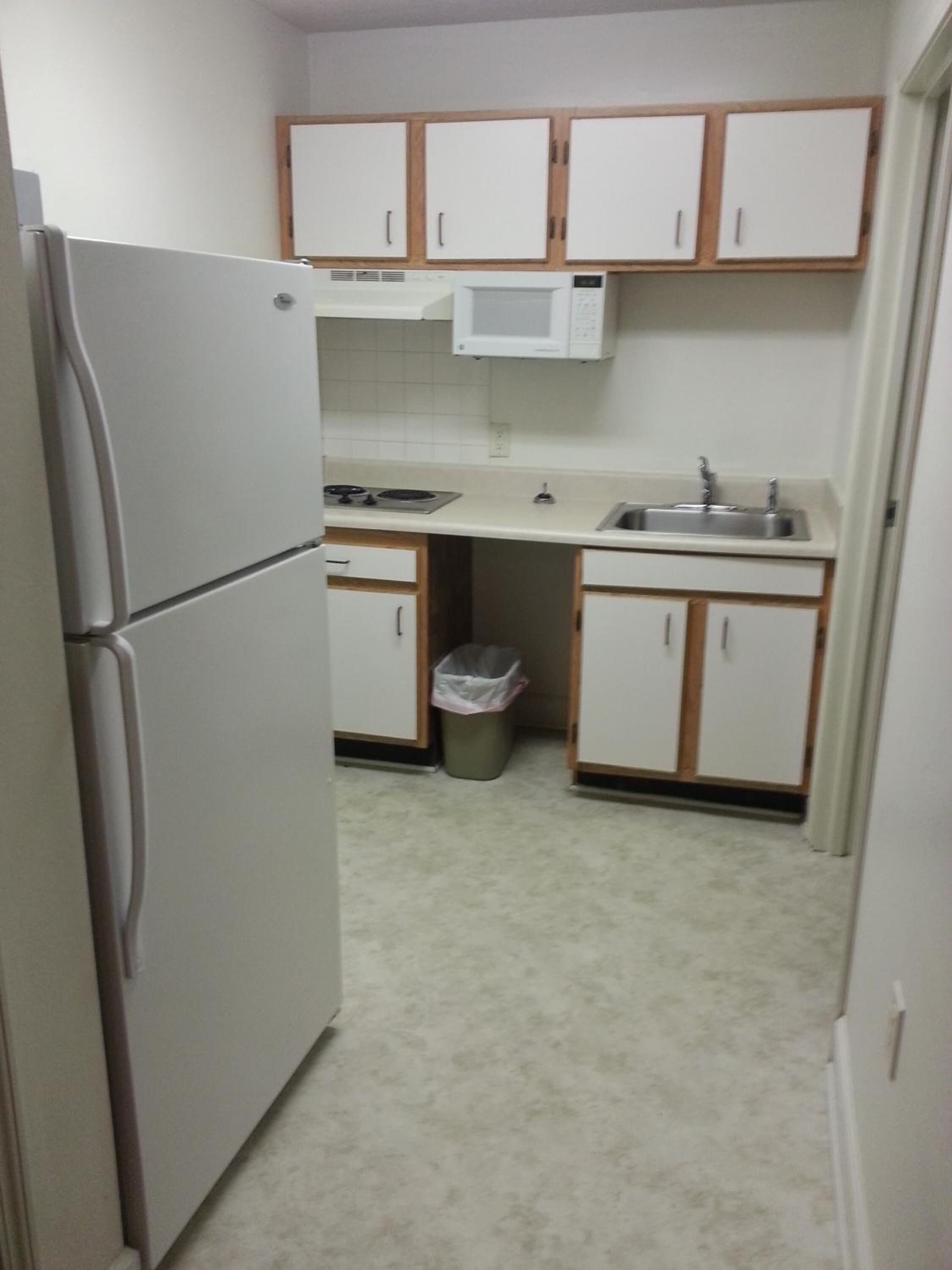 Una cocina compacta equipada con refrigerador, microondas, pileta y basurero.