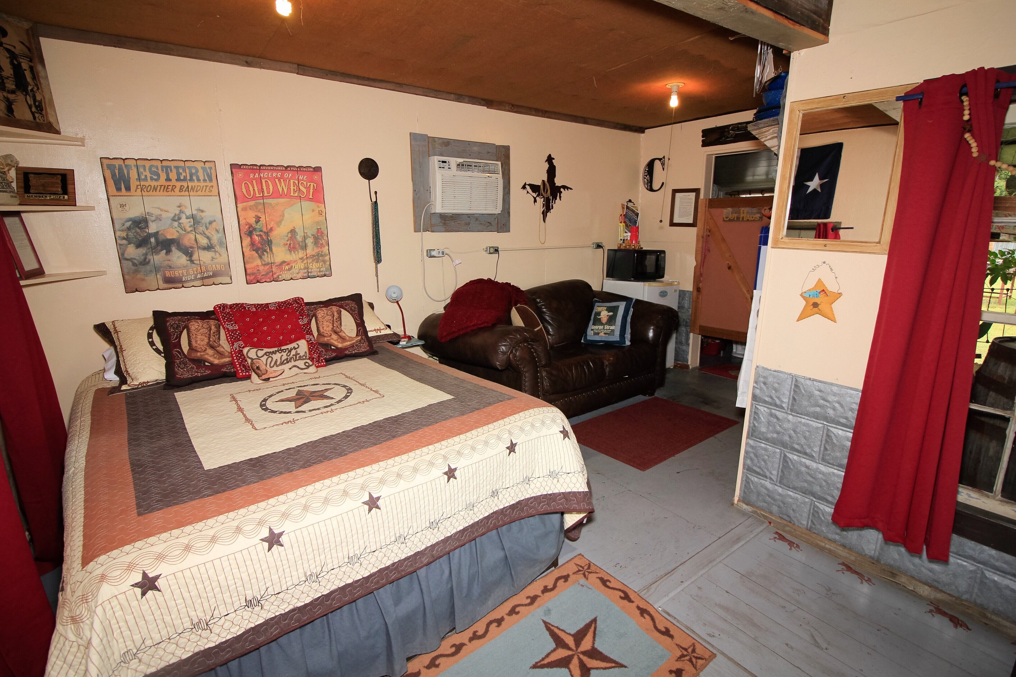A room with a large bed, a leather couch, and a small TV. There are posters on the wall and a window with curtains.