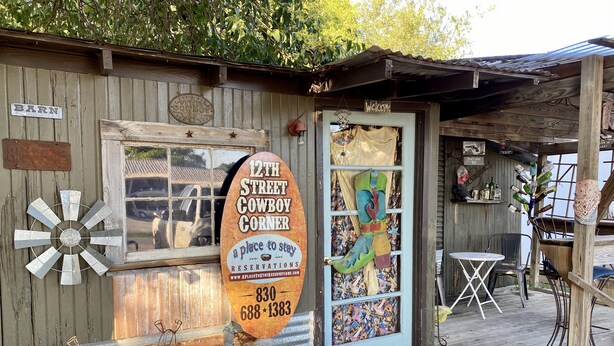 Un edificio rústico con un cartel que dice "12th Street Cowboy Corner" y un felpudo.