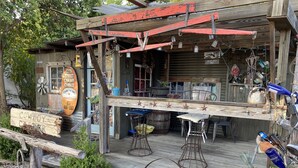 Un edificio de madera rústico con un porche, un letrero que dice "Cowboy Corner" y varios objetos exhibidos en el exterior.