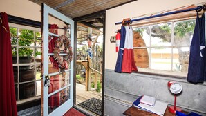 Una habitación con puerta de madera, ventana con cortinas, escritorio con lámpara y vistas al exterior.