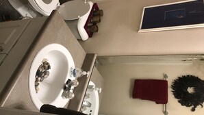 A bathroom with a toilet, sink, and mirror. There is a towel rack with a red towel and a wreath on the wall.