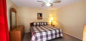 A bedroom with a bed, a nightstand, a lamp, a ceiling fan, a mirror, and a painting on the wall.