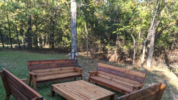 Un’area salotto esterna in legno con panche e un tavolo, immersa tra gli alberi.