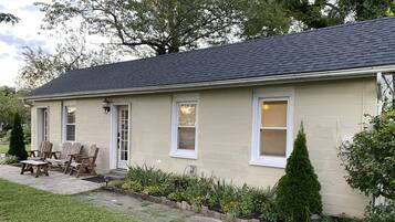 A single-story house with a dark roof, beige exterior walls, and a front porch with wooden chairs.