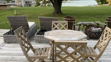 Relax on the deck surrounded by a lush lawn and a majestic tree, with a table and chairs perfect for outdoor dining.