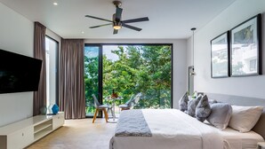 Une chambre moderne avec un grand lit, un ventilateur de plafond, une télévision et un balcon équipé d’une table et de chaises.