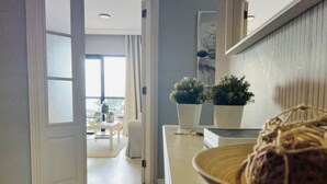 Un interior moderno con un pasillo que conduce a un comedor. Hay dos plantas en macetas sobre una encimera, un llavero y una cesta tejida.