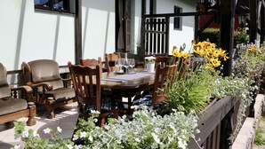 An outdoor patio with a wooden table and chairs, surrounded by potted plants and flowers. - Holiday home Lipno, Slupečná (Lipno nad Vltavou)
