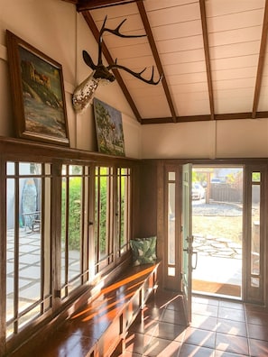 A room with a wooden bench, a deer head mounted on the wall, and a painting.